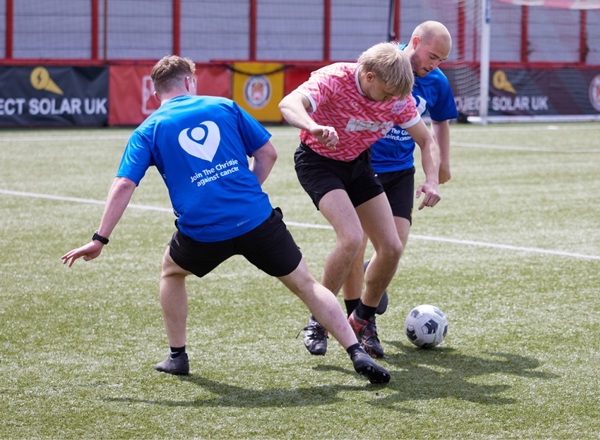 A photo of 3 people playing football, 2 people wearing Christie Charity t-shirts.