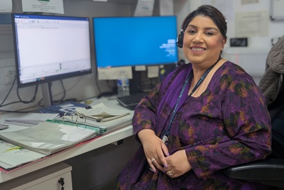 A photo of Sumaira Javed, switchboard operator at The Christie, sitting in front of 2 computer screens and wearing a phone headset.