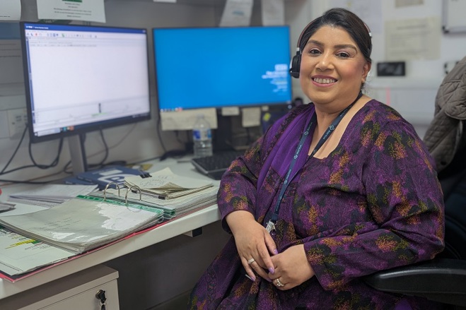 A photo of Sumaira Javed, switchboard operator at The Christie, sitting in front of 2 computer screens and wearing a phone headset.