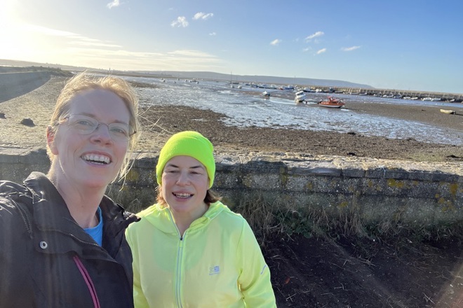 A photo of Claire White and Chantal Neal standing at the coast with the tide out; small boats can be seen in the background.
