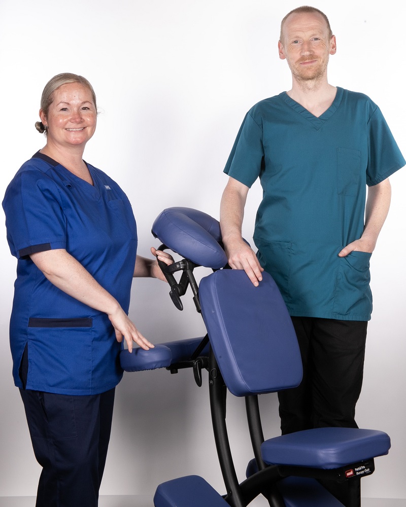 A photo of Eileen Hackman and Trainee Integrative Therapist Anthony Preston in uniform standing either side of a therapy chair.