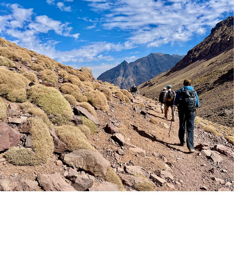 A photo of a trek in Morocco with hikers in the foreground and mountains in the background.
