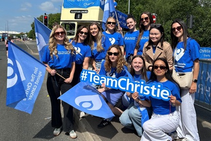A group of colleagues from Hill Dickinson wearing Christie Charity t-shirts at a sporting event and standing in front of a Christie Charity open-top bus.