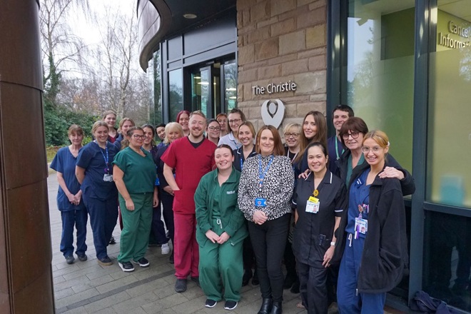 A photo of Christie at Macclesfield staff celebrating the centre's third anniversary, standing outside the centre's entrance.