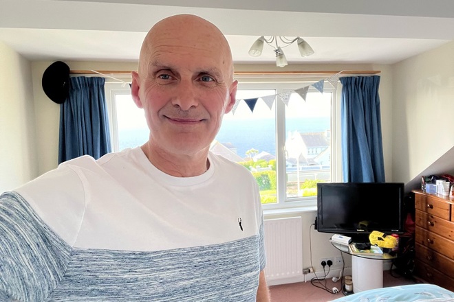 A photo of Christie prostate patient Andy Fleet in a a bedroom with a window and bunting behind him.