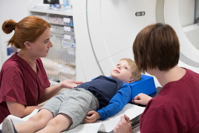 A photo of a child patient being treated with radiotherapy by 2 radiographers.