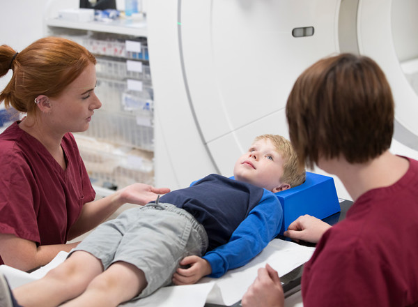 A photo of a child patient being treated with radiotherapy by 2 radiographers.