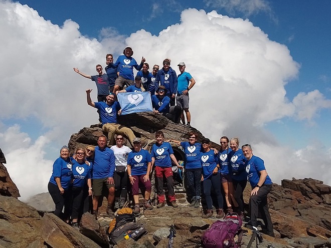 A photo of a large group of fundraisers wearing Christie Charity t-shirts and holding a Christie Charity t-shirt on a mountain top as part of the Spanish 3 Peaks Trek.