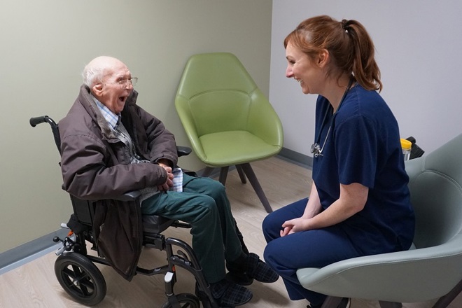 A photo of Christie patient Arthur Oarton sitting in a wheelchair opposite advanced clinical practitioner Laura Bradley, who is sitting in a chair.