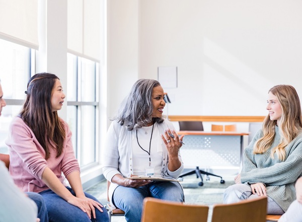 A photo of 3 women and 1 man sitting around in a circle and talking.