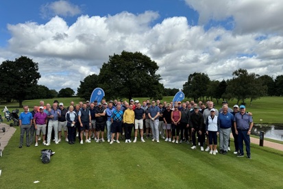 A photo of a large groups of golfers standing at a golf course, with Christie Charity banners in the background.