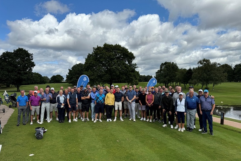 A photo of a large groups of golfers standing at a golf course, with Christie Charity banners in the background.