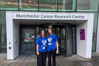 A photo of Lucy Graves and Ella Havard wearing Christie Charity t-shirts and standing outside the Manchester Cancer Research Centre.