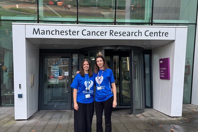 A photo of Lucy Graves and Ella Havard wearing Christie Charity t-shirts and standing outside the Manchester Cancer Research Centre.