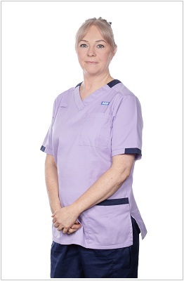 A photo of a clinical healthcare assistant or support worker wearing a uniform in lilac with navy trim.
