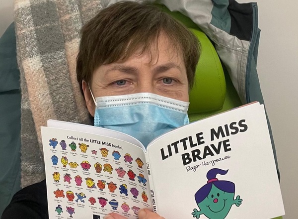 A photo of Christie patient Michelle Gidion wearing a disposable face mask and reading the book 'Little Miss Brave'.