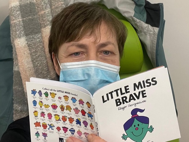 A photo of Christie patient Michelle Gidion wearing a disposable face mask and reading the book 'Little Miss Brave'.