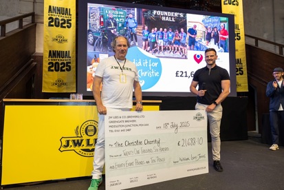 A photo of a man from J.W. Lees Brewery and John from The Christie Charity standing on a stage and holding a big cheque for The Christie Charity.