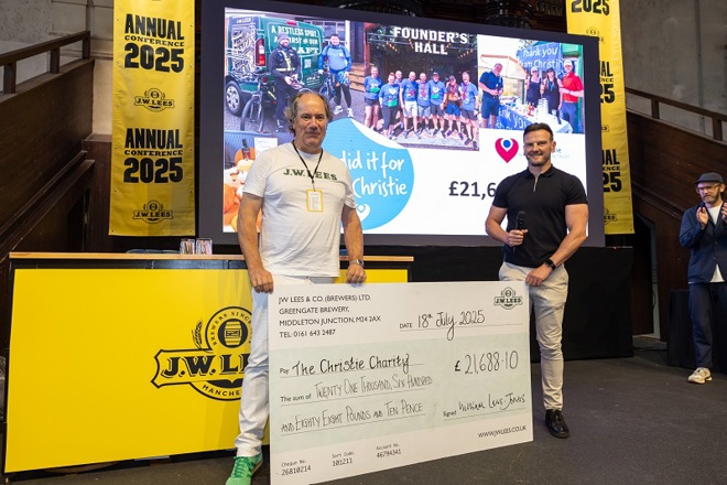 A photo of a man from J.W. Lees Brewery and John from The Christie Charity standing on a stage and holding a big cheque for The Christie Charity.