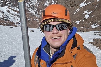 A photo of Christie fundraiser Matt Heywood on top of snowy Mount Toubkal wearing a hard hat and holding an ice pick.