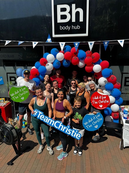 A photo of Amanda White and 11 other people standing outside a gym called BH Body Hub. The group is standing underneath a balloon arch and members of the group are holding signs reading 'I did it for The Christie', 'We did it for The Christie' and '#TeamChristie'.