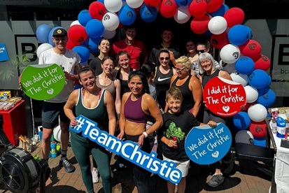 A photo of Amanda White and 11 other people standing outside a gym called BH Body Hub. The group is standing underneath a balloon arch and members of the group are holding signs reading 'I did it for The Christie', 'We did it for The Christie' and '#TeamChristie'.
